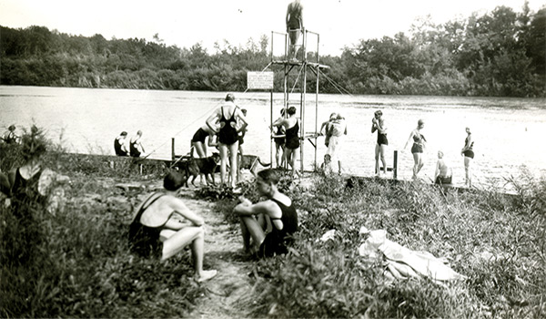 Figure 3. Swimmers at university dock, circa 1920s to early 1930s. The sign on the diving tower reads, &ldquo;Notice: Anyone swimming or bathing here without permission will be prosecuted for trespassing. Man. Agric. College.&rdquo;