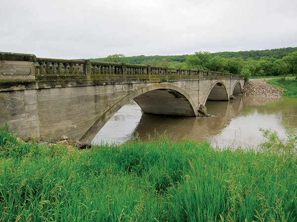 An impressive triple-arch concrete bridge over the Assiniboine River, in the village of Millwood in the Rural Municipality of Russell, was built in 1920, replacing an earlier wooden structure. Aside from minor damage to the balusters of its railings, it is in good condition.