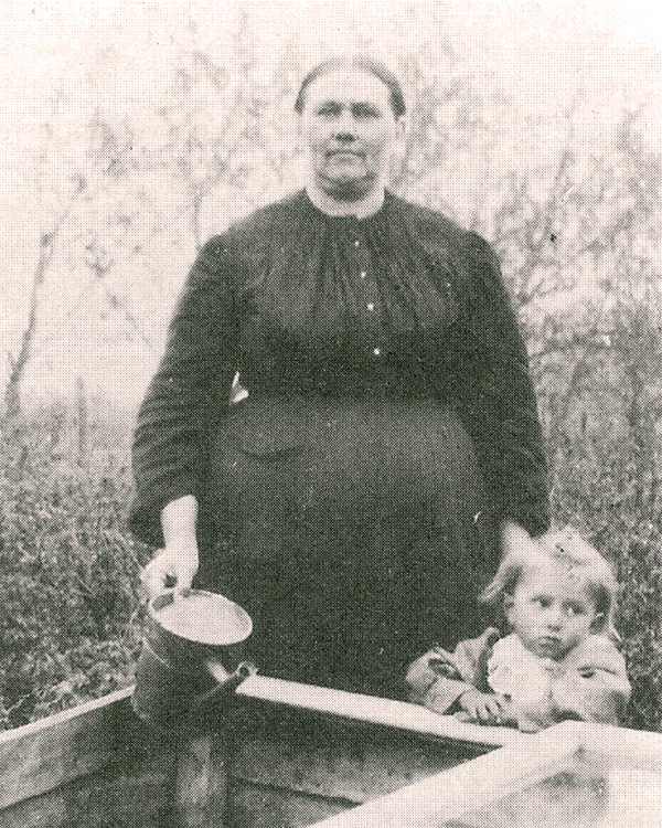 Pioneer midwife Anna Toews (1868–1933) with daughter Margaret standing beside a cold frame used to start plants, circa 1912.