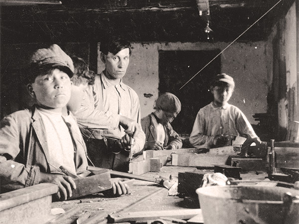 Indigenous boys use saws, planes, and other tools in a carpentry class at the residential school, circa 1910.