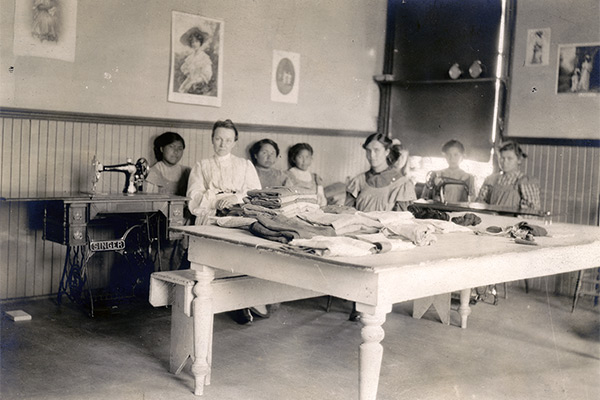 Indigenous girls with their instructor in a sewing class at the Brandon Residential School, circa 1900.