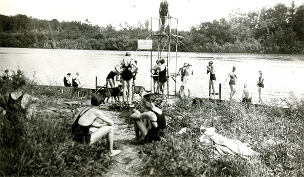 Figure 3. Swimmers at university dock, circa 1920s to early 1930s. The sign on the diving tower reads, “Notice: Anyone swimming or bathing here without permission will be prosecuted for trespassing. Man. Agric. College.”