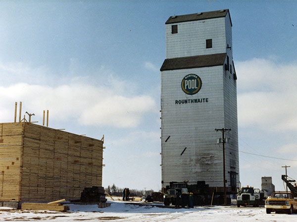 The former Manitoba Pool grain elevator B from Rounthwaite at its new site in Nesbitt, with a new crib annex under construction in the foreground and the United Grain Growers elevator in the right background