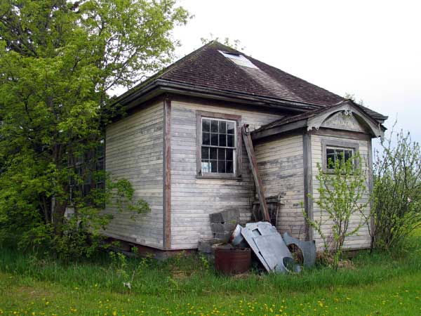 The original Wheathill School building in a farmyard at N50.83213, W97.53611 with the name still visible above the entrance vestibule