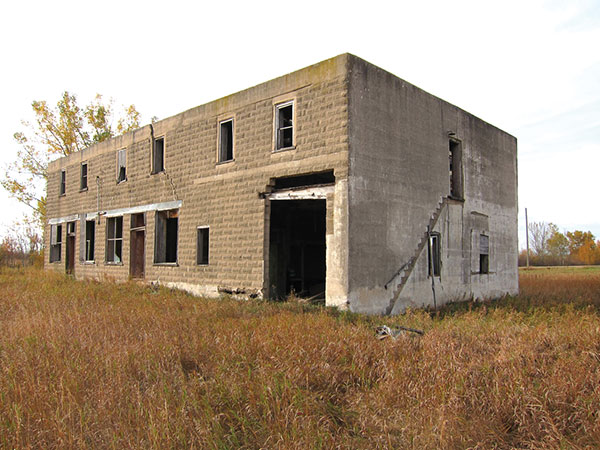 Kilkenny General Store (Broomhill, RM of Albert). This two-storey building was built for William Kilkenny and his brother John. In its heyday, the Kilkenny store was the centre of the community. A hand-operated gasoline pump sat at the south end, in front of an entrance to the store and post office, with an implement agency and garage at the north end. Rooms on the upper storey were used as residential space. The business was operated by a succession of Kilkennys until it closed in September 1964. The building’s east and south walls are made from patterned concrete blocks. The roof is gone and the interior floors have failed in several places but, otherwise, the concrete structure is largely intact. Pressed metal wall and ceiling panels from the interior have been salvaged by a grandson of the last owner and are available for purchase.