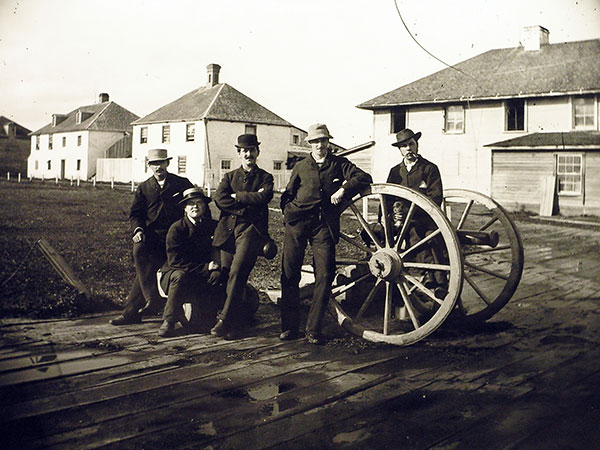 Unidentified men posing around cannons inside Upper Fort Garry